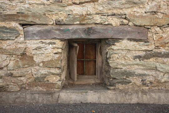 Close up of an ancient stone wall with a small rustic wooden window and a weathered timber lintel.