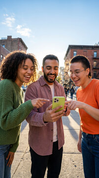 Animated friends pointing at smartphone screen on sunlit city sidewalk together