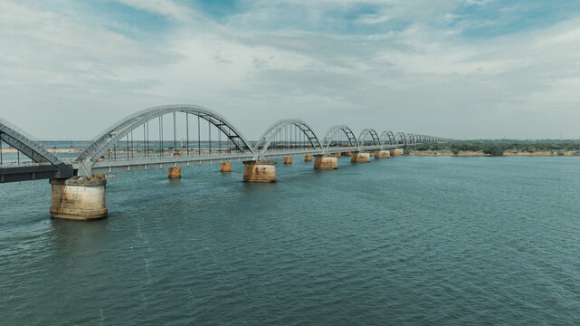 Aerial view of the Godavari Arch Bridge spanning the wide Godavari River with its distinctive steel arches and concrete piers under a cloudy sky in Rajamahendravaram, Andhra Pradesh, India.