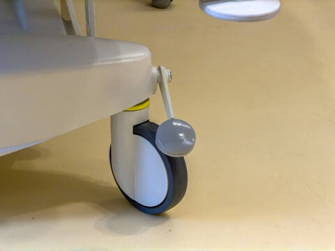 Close-up of hospital bed caster wheel and brake pedal on smooth beige clinical floor