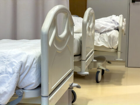 Two empty adjustable hospital beds with rumpled linens in an unoccupied clinical room