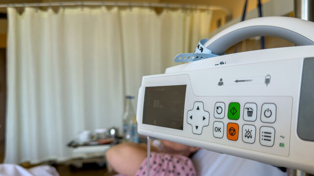 Electronic infusion pump beside a resting patient in a hospital room, closeup view