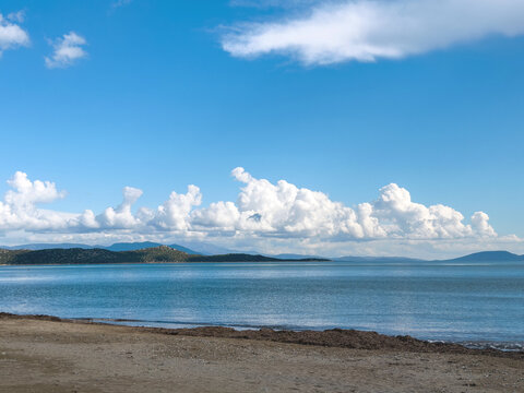 Sandy shore and calm blue water under towering clouds in Schinias, Attica, Greece