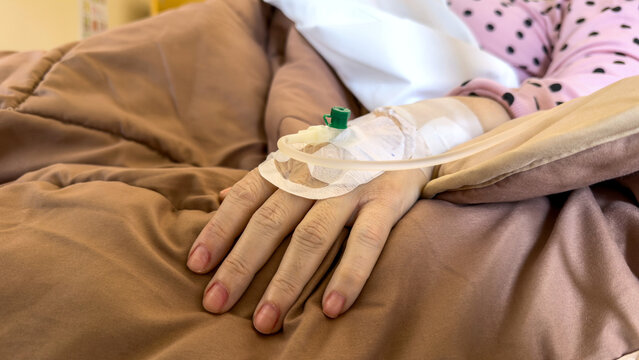 Intravenous cannula attached to patient hand resting on hospital bed closeup