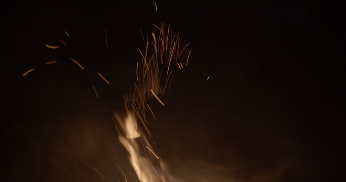 Bright fire with glowing sparks and embers rising against the night sky