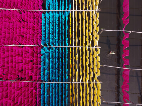 Aerial view of vibrant pink, blue, and yellow fabrics hanging to dry on bamboo frames over water in Narayanganj, Dhaka, Bangladesh.