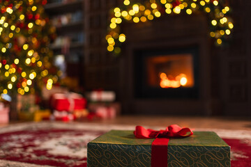 Fototapeta premium Green gift box in classical Christmas decorated interior living room library with fireplace. Christmas gift near fir tree on Christmas eve. Modern classic style interior design apartment. Christmas