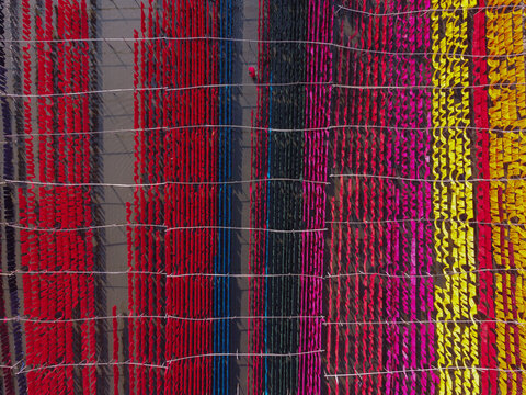 Aerial view of vibrant colorful fabrics hanging to dry on bamboo frames in a textile dyeing facility in Narayanganj, Dhaka, Bangladesh.
