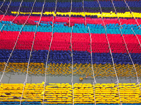 Aerial view of vibrant colorful fabrics hanging to dry on bamboo racks above the water at a textile dyeing factory in Narayanganj, Dhaka, Bangladesh.