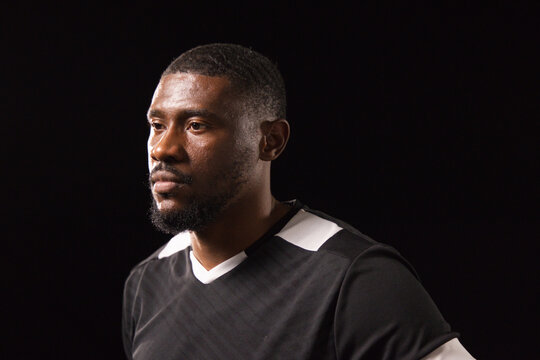 African man posing under studio lighting wearing black athletic shirt with white trim