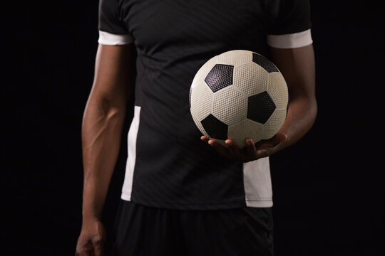 Mid-adult African man holding black-and-white soccer ball standing in studio wearing black jersey