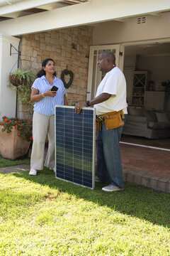 African American homeowner and technician discussing solar panel on porch, woman holding smartphone