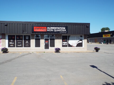 Gatineau, Quebec, Canada &ndash; June 24, 2026: A storefront for "Alimentation Mon Quartier" with branded window graphics and flower pots in a parking lot on a sunny day at 130 Bd Gr&eacute;ber Unit number 7.