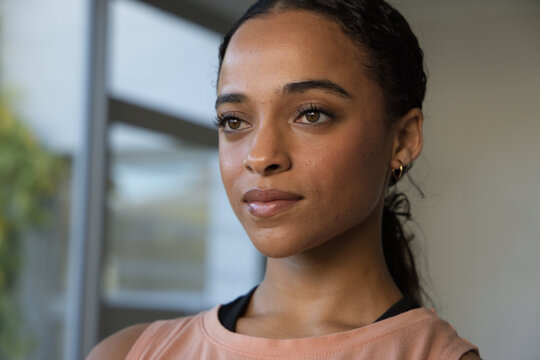 African American adult woman gazing out glass window at home, wearing peach sleeveless top