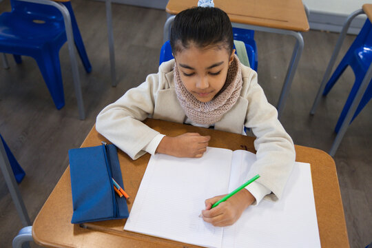 African American youth female student writing in lined notebook at class desk holding green pencil