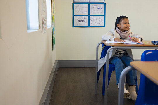 African American child sitting school desk writing notebook holding pink pen in coat, copy space