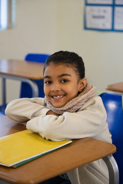 African American school-age girl sitting at desk at school, wearing scarf, smiling, yellow notebook