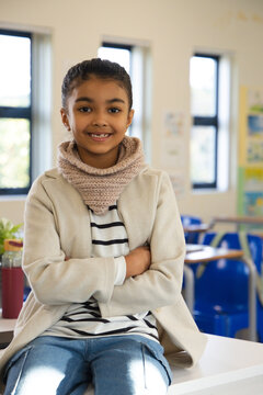 African American schoolgirl sitting on white table wearing beige cowl, maroon bottle nearby