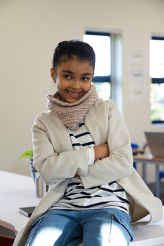 African American youth female sitting on table in classroom, wearing coat and scarf, laptop visible