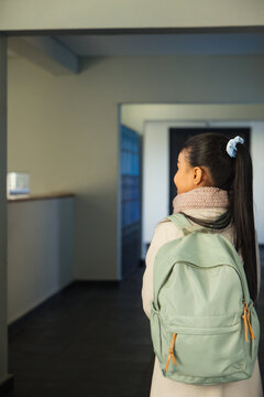 African American teenage girl standing in school corridor with coat scarf mint backpack, copy space