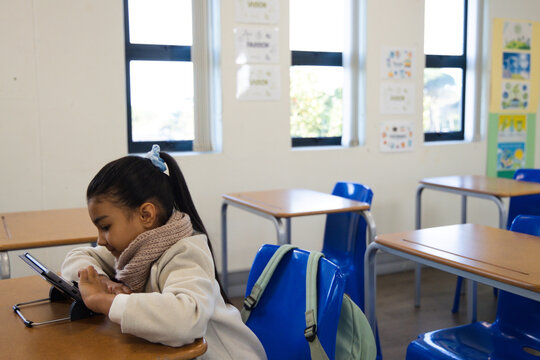African American girl leaning on desk using tablet on folding stand in classroom, copy space