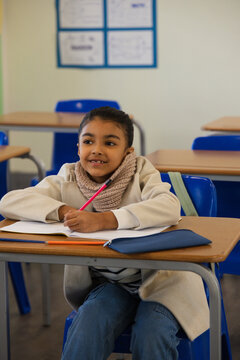 African American child sitting in classroom on blue chair at desk holding pink pencil over notebook