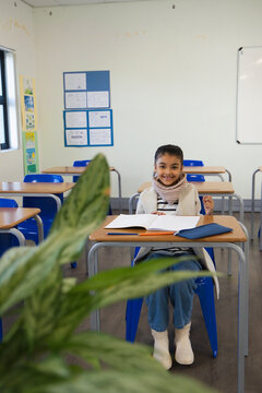 African American child student smiling at desk in class with notebook, blue folder and chunky scarf
