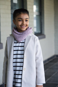African American teenage girl standing and smiling on covered walkway wearing long coat and scarf