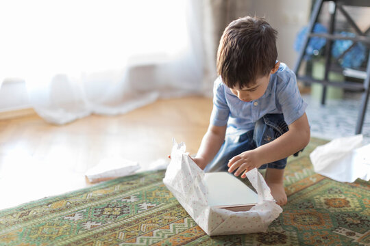 Young Boy crouching on the floor in a living room unwrapping a wrapped birthday gift