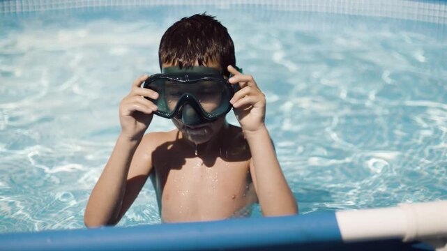 Little boy putting on goggles and diving into swimming pool during summer vacation