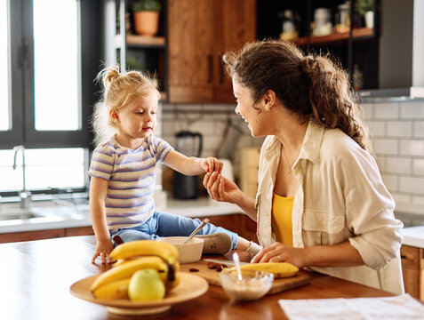 Portrait of a mother and daughter preparing and eating breakfast and having fun in the kitchen at home