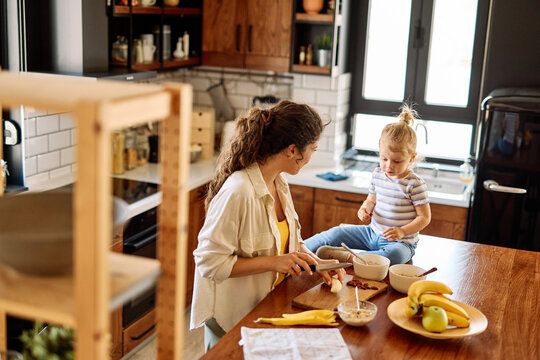 Portrait of a mother and daughter preparing and eating breakfast and having fun in the kitchen at home