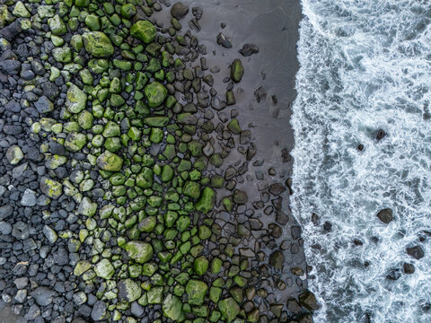 Aerial view of Praia do Areal de Santa Barbara with moss-covered volcanic rocks and crashing ocean waves along the coastline in Ribeira Grande, Acores, Portugal.