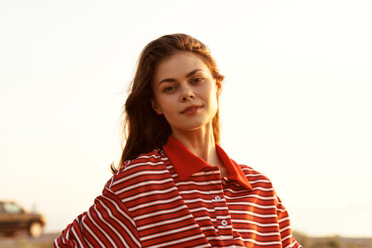 Smiling woman in a red striped polo outdoors at sunset. Lifestyle portrait emphasizing casual fashion, warmth, and relaxed confidence in natural light.