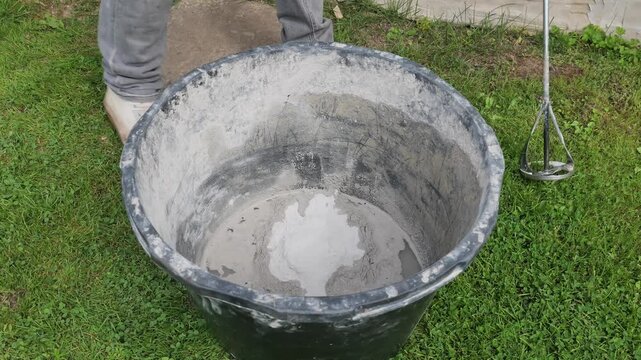 Worker Mixing Plaster With Water in a Bucket Outdoors