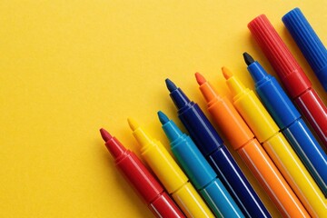 Fototapeta premium Colorful felt tip pens without caps lie on bright yellow background. Group of many rainbow markers arranged in diagonal line. Stationery tools for drawing, art project, school education office work.