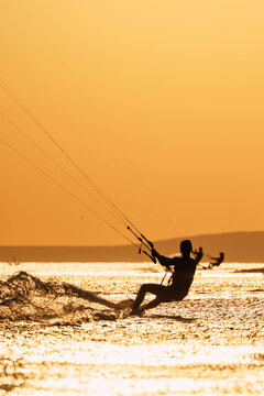 Kite surfer riding across sparkling waves during golden sunset