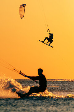 Kite surfer riding on sea with a kite overhead at sunset