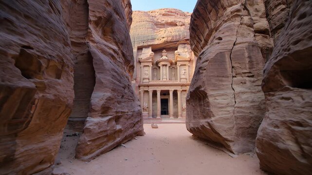 The ancient Treasury of Petra gradually appears at the end of the narrow Siq canyon as the camera moves through the rose-red sandstone passage in Jordan.