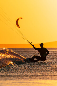 Kite surfer carving through the waves with a kite against a glowing sunset