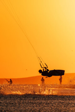 Kite surfer performing an aerial trick above the water at golden sunset