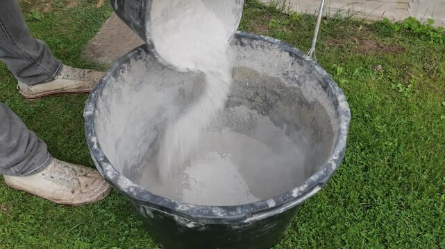 Worker Pouring Dry Plaster Mix Into Water Before Mixing