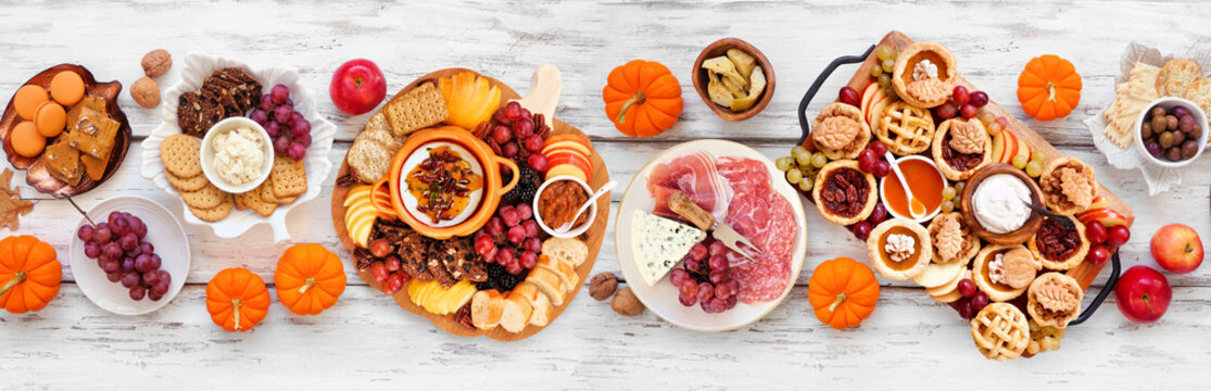 Autumn or Thanksgiving appetizers, sweets and grazing boards. Above view table scene on a white wood banner background. Pumpkin and apple snacks, charcuterie, pies, desserts.