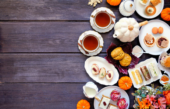 Fall theme afternoon tea side border against a dark wood background. Pumpkin and apple theme savory finger foods, sandwiches, scones, and desserts. Top down view with copy space.