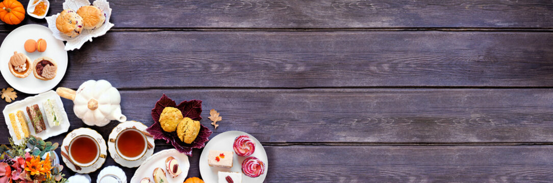 Autumn theme afternoon tea corner border against a dark wood banner background. Pumpkin and apple theme savory finger foods, sandwiches, scones, and desserts. Above view with copy space.