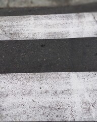 Fototapeta premium Close-up of a weathered asphalt and concrete surface with contrasting black and white horizontal painted stripes. The rough pavement texture creates a minimalist geometric pattern suitable for urban b