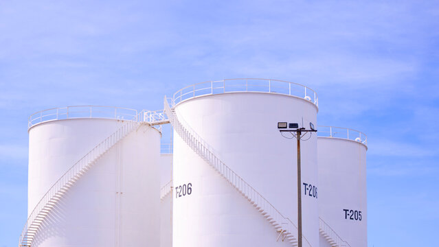 Group of storage fuel tanks in petroleum industrial oil refinery area against blue sky background