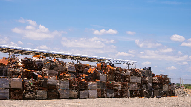 Industrial scrap metal yard with stacks of rusty iron waste and materials waiting for recycling under blue sky background.