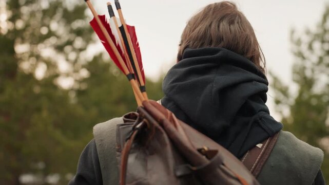 A man is meticulously preparing to shoot an arrow in a serene forest setting, captured from an over-the-shoulder perspective. The scene highlights his focused concentration as he readies.