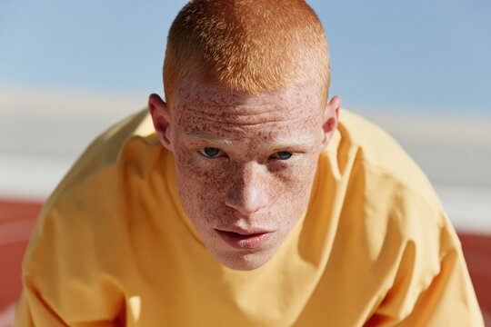 Closeup intense portrait of a freckled redhead athlete crouched on track for sports banner background and athletic training poster design